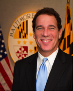 Man smiling in front of Baltimore flags.