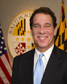 A man in a suit poses with a Maryland flag background.