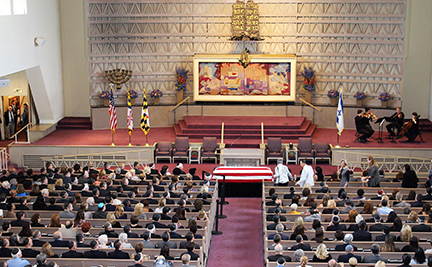 A large audience watches a stage with a colorful backdrop and trophies.
