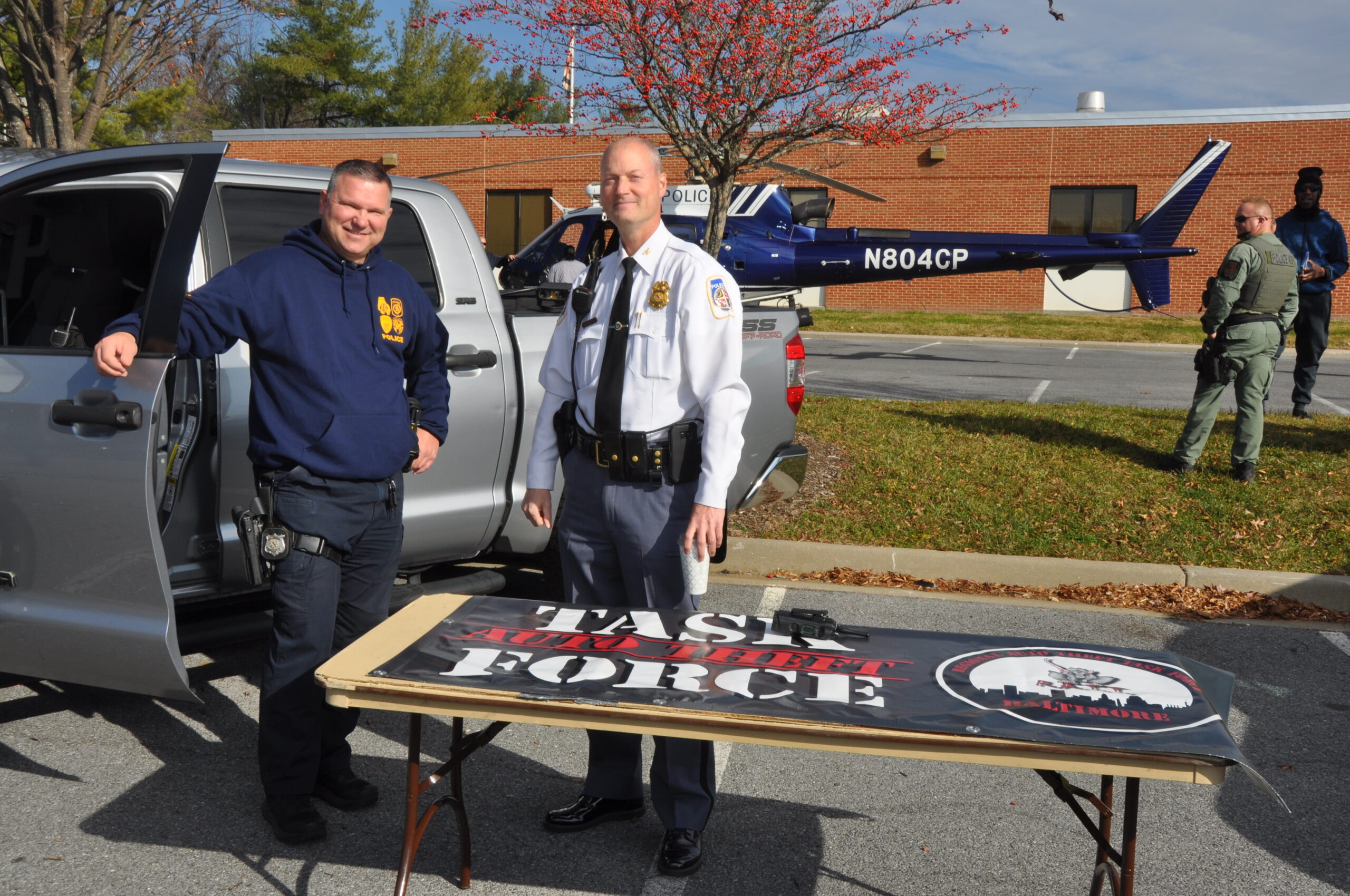 Two men standing by a table with a 'VOTE' sign outdoors.