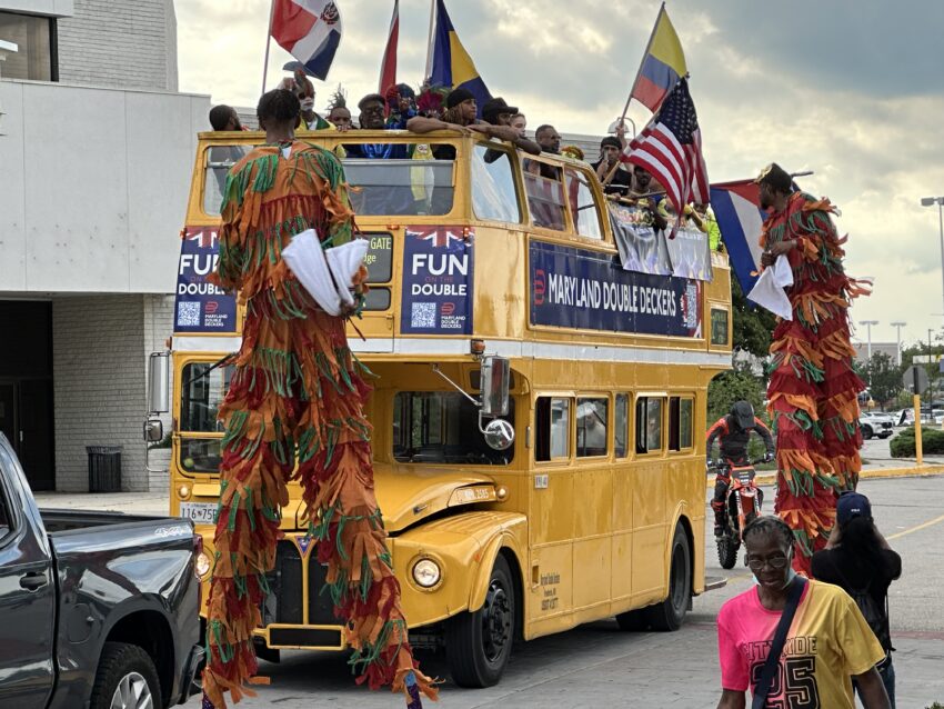 Colorful parade with performers on stilts and a vintage double-decker bus.