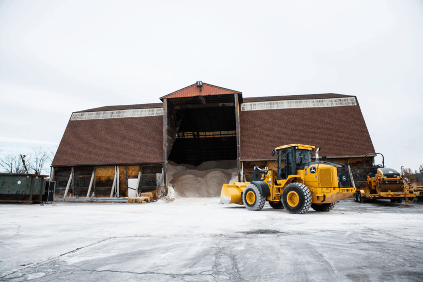A large yellow wheel loader parked outside a barn on a snowy day.
