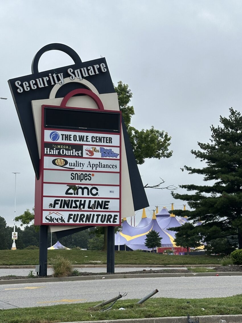 Shopping plaza sign listing various businesses on a cloudy day.
