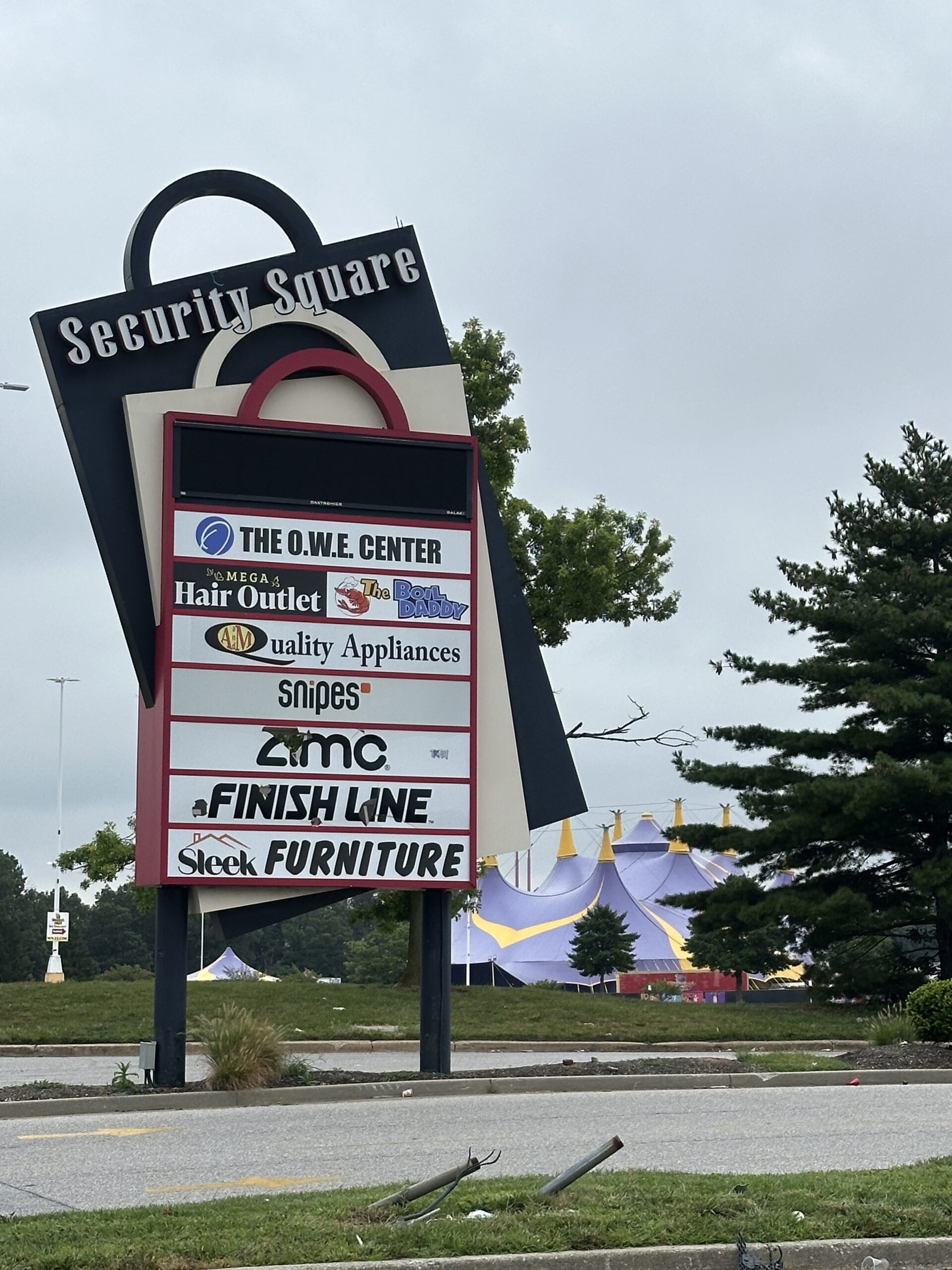 Shopping plaza sign listing various businesses on a cloudy day.