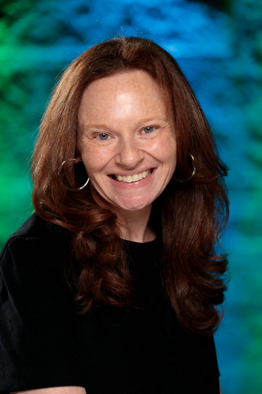 Smiling woman with long red hair against a blue-green background.